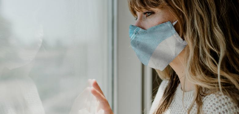 Mujer con mascarilla mirando por la ventana